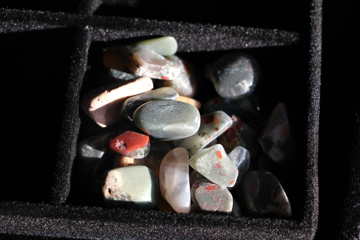 Polished jasper stones in black velvet jewelry box compartment under soft light