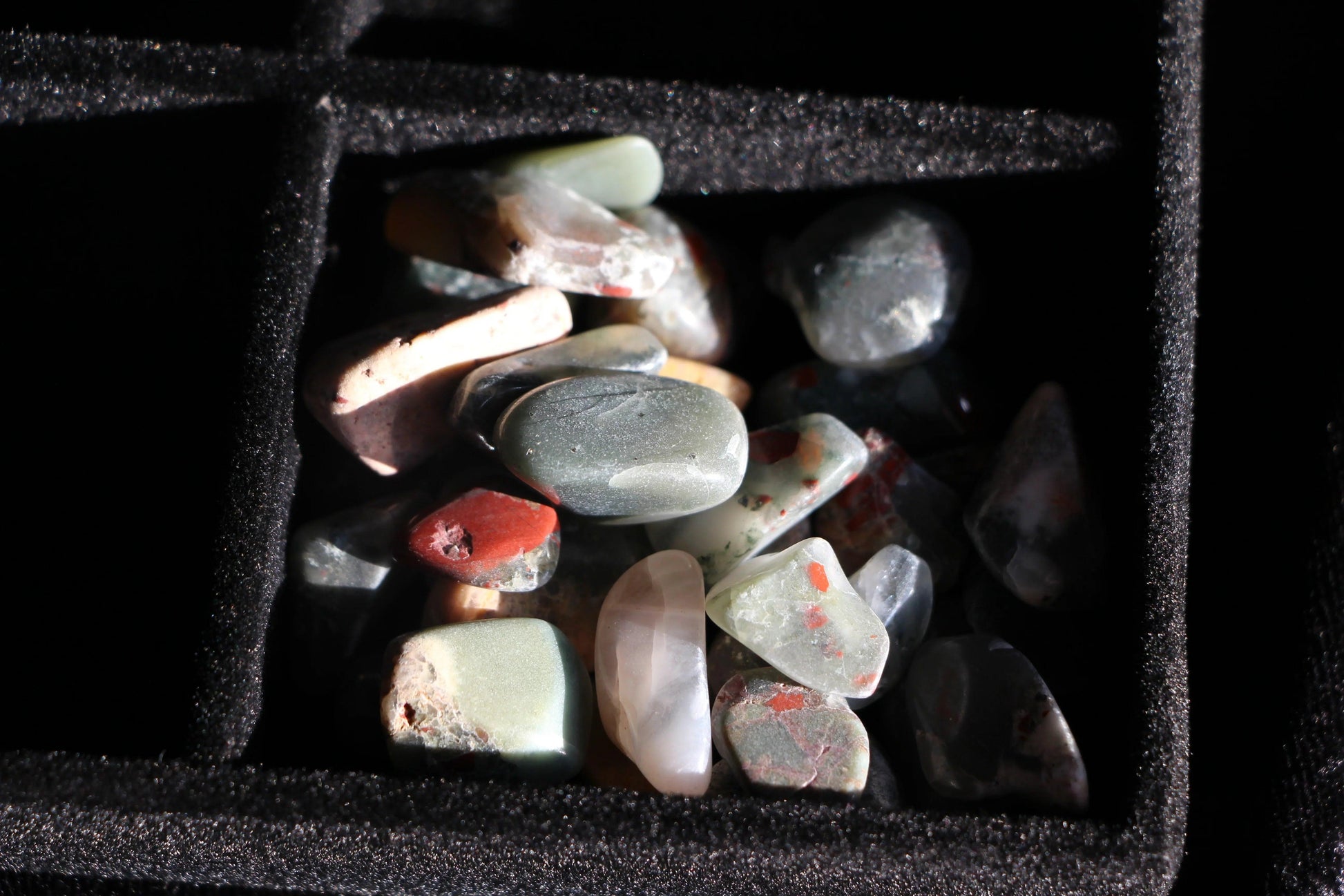 Polished jasper stones in black velvet jewelry box compartment under soft light