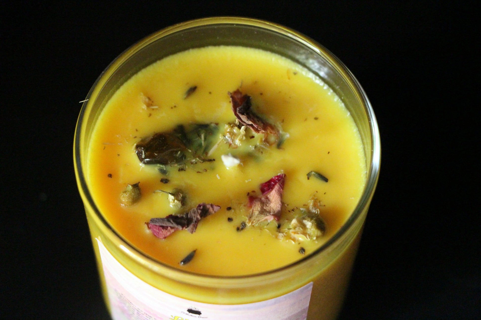 Yellow crystal candle with dried herbs in glass jar on black background, Witches' Brew