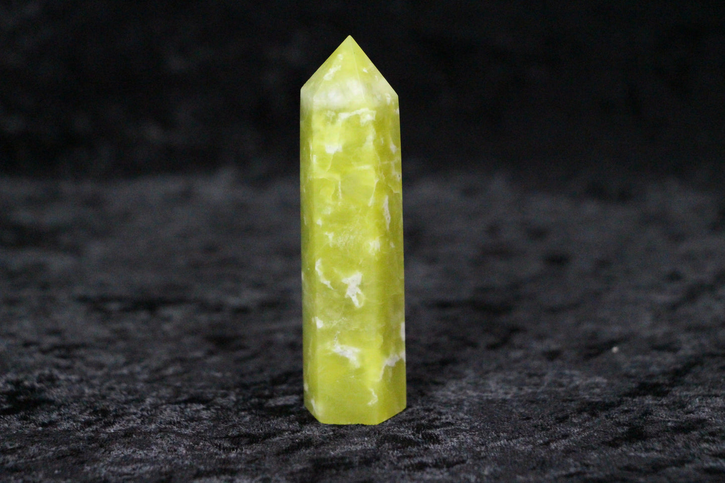 Polished yellow-green serpentine crystal point standing on black textured surface