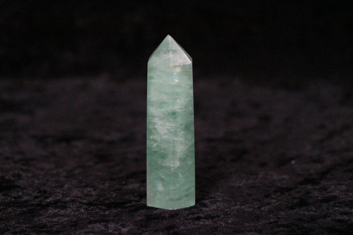Green fluorite crystal point on black textured surface with dark background