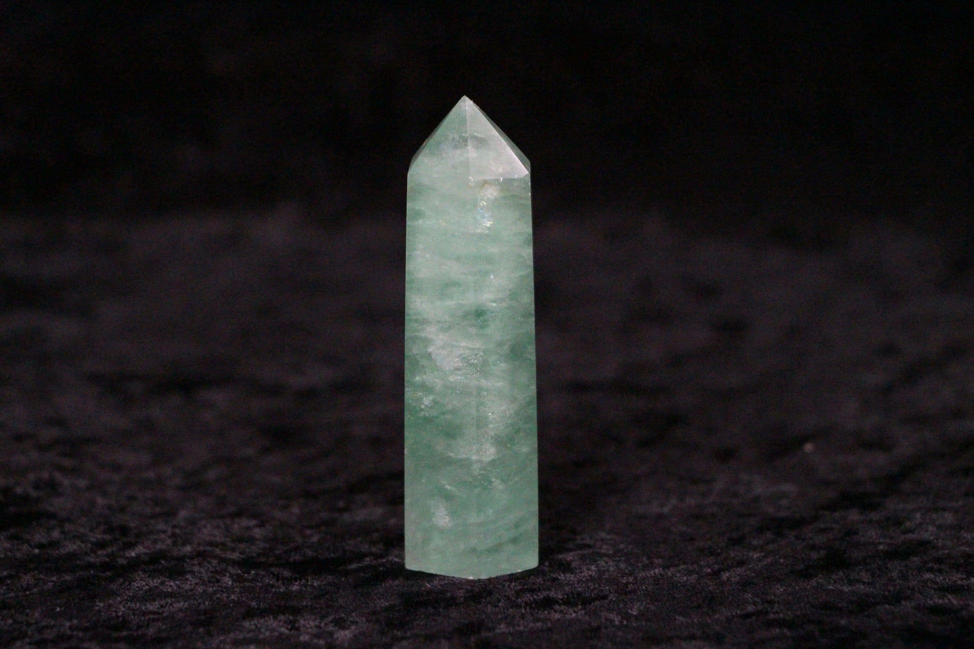 Green fluorite crystal point on black textured surface with dark background