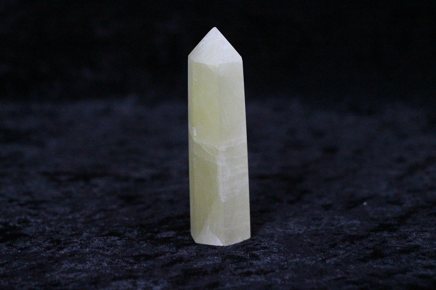 Polished light yellow calcite crystal point standing on black textured surface