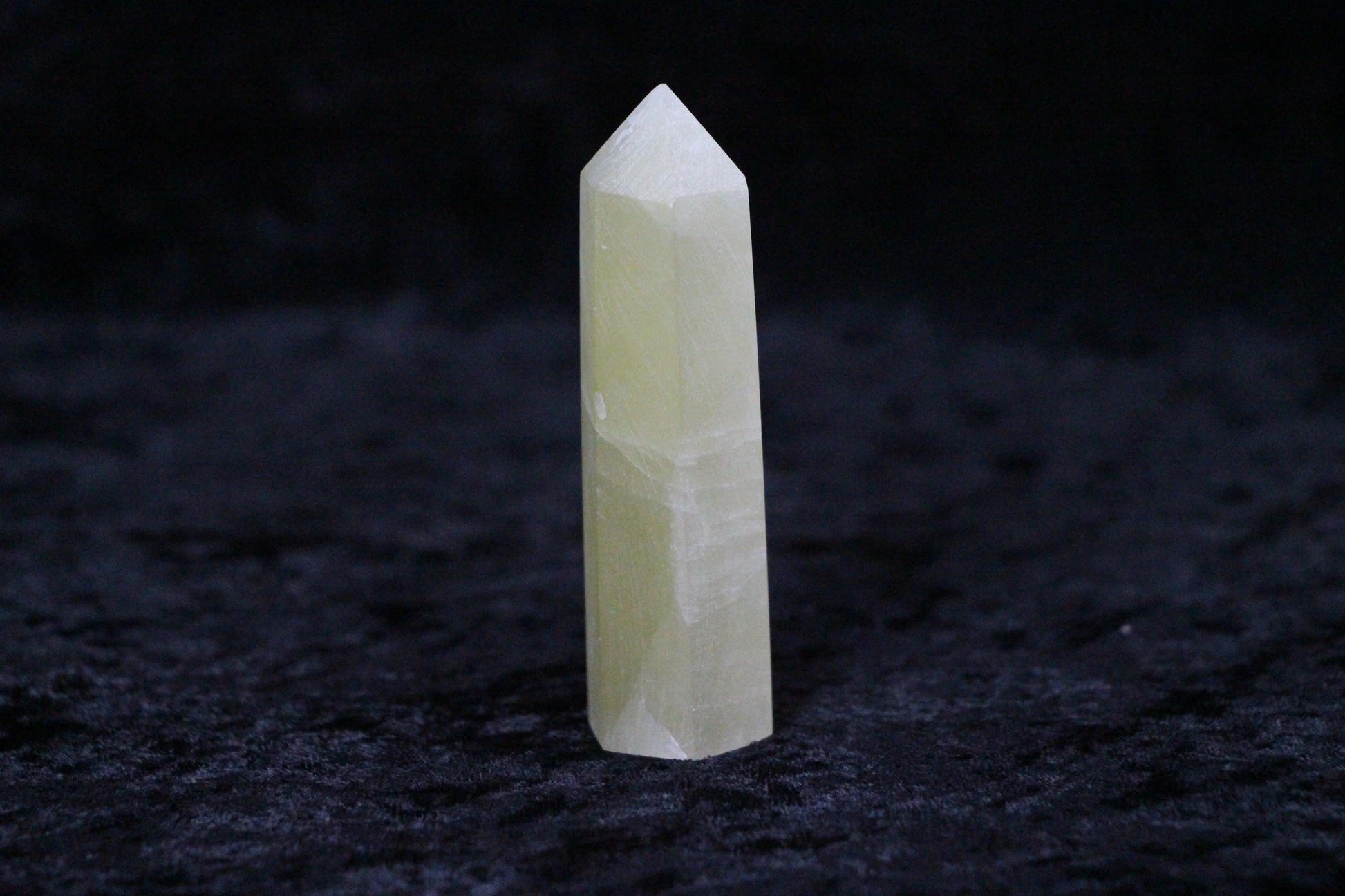 Polished light yellow calcite crystal point standing on black textured surface