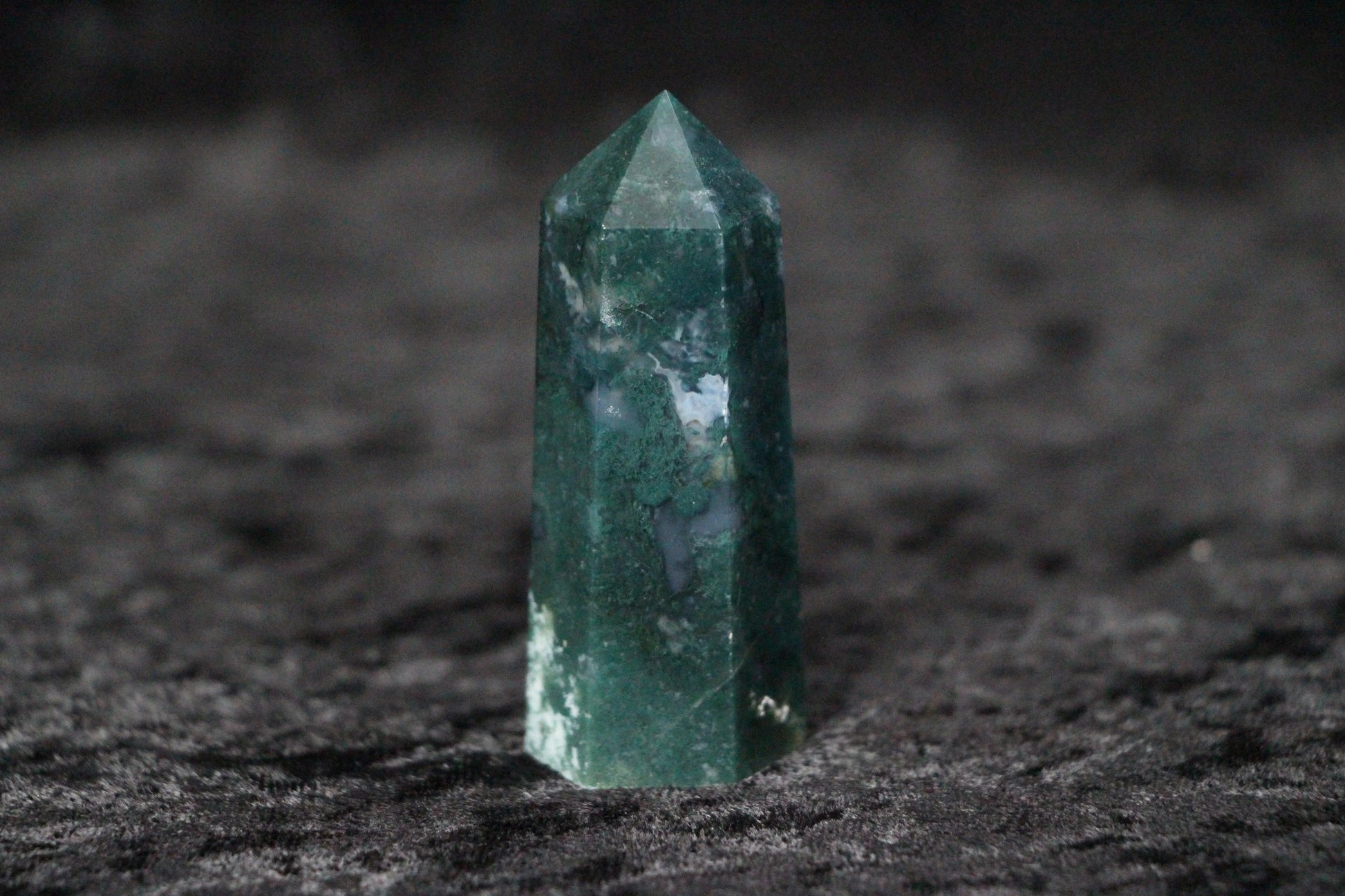 Green moss agate crystal point standing on dark textured surface with natural white inclusions
