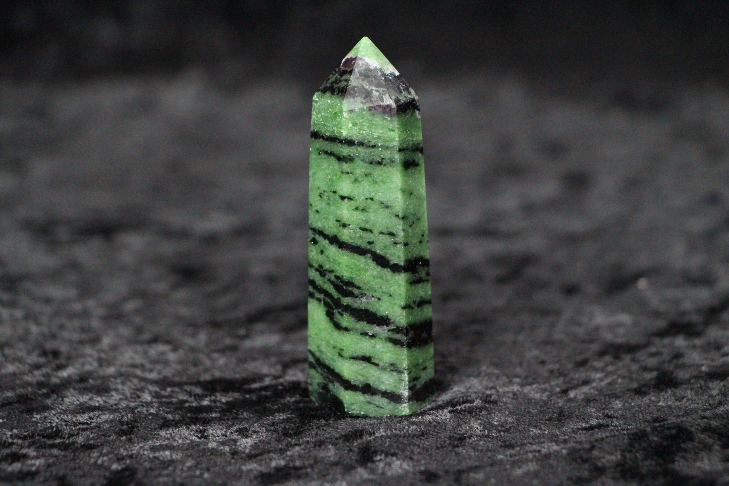 Green and black striped gemstone tower standing on dark textured surface