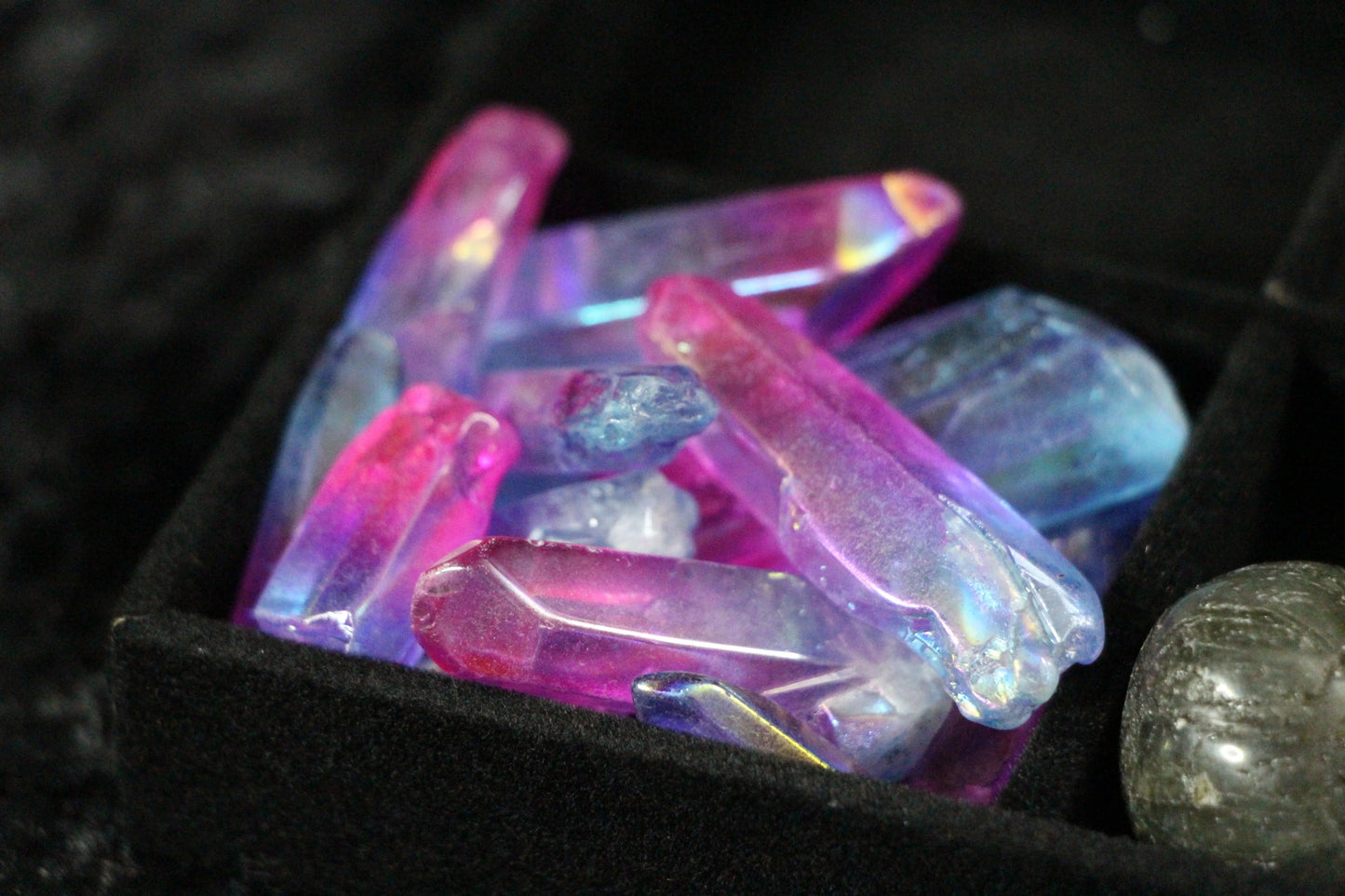 Iridescent pink and blue crystal points in a black velvet tray, modern witch ritual tools