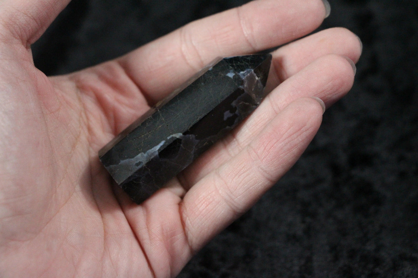 Hand holding polished black and dark purple crystal point with marbled patterns