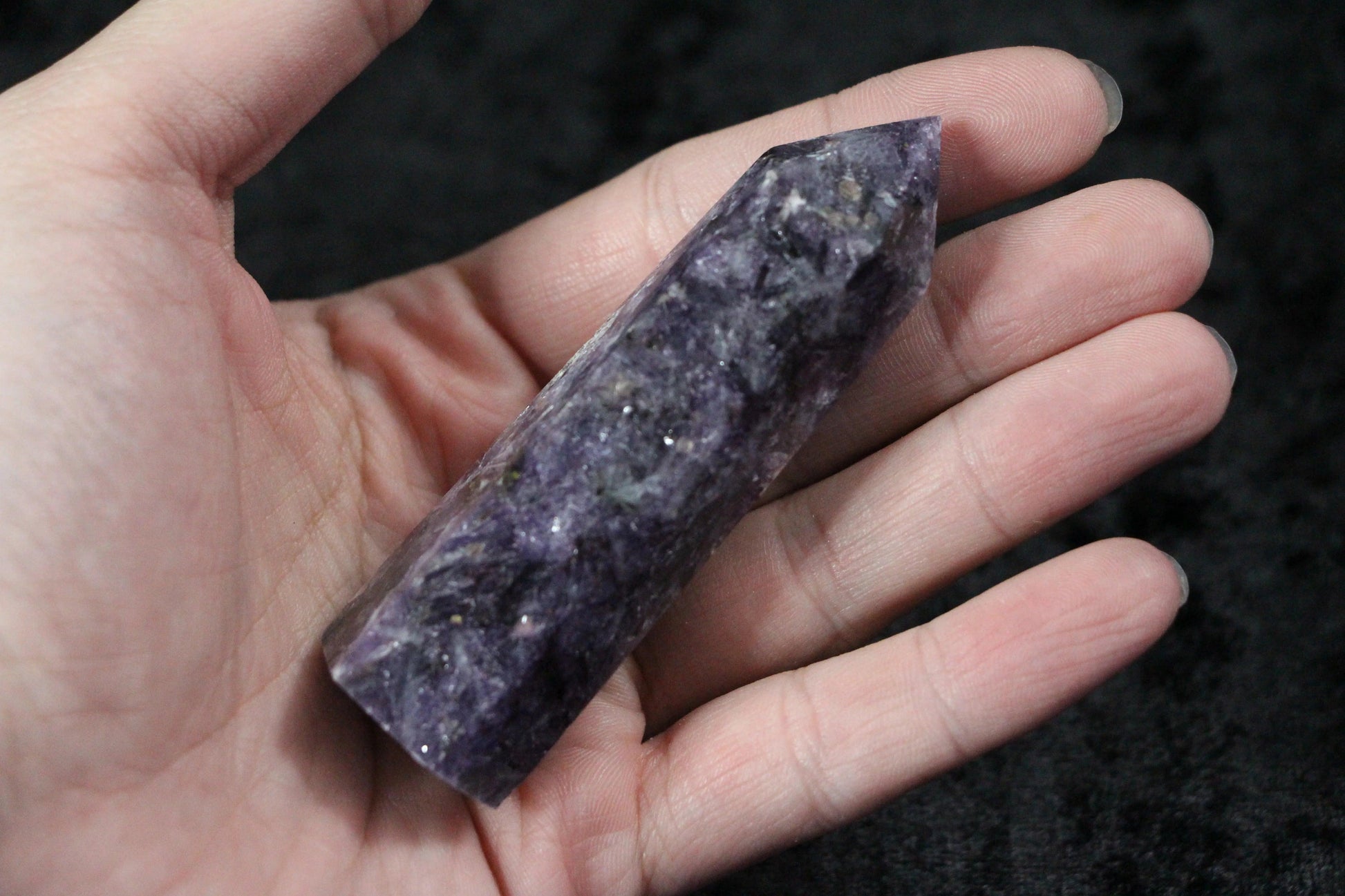 Hand holding a polished purple amethyst crystal point on a black background