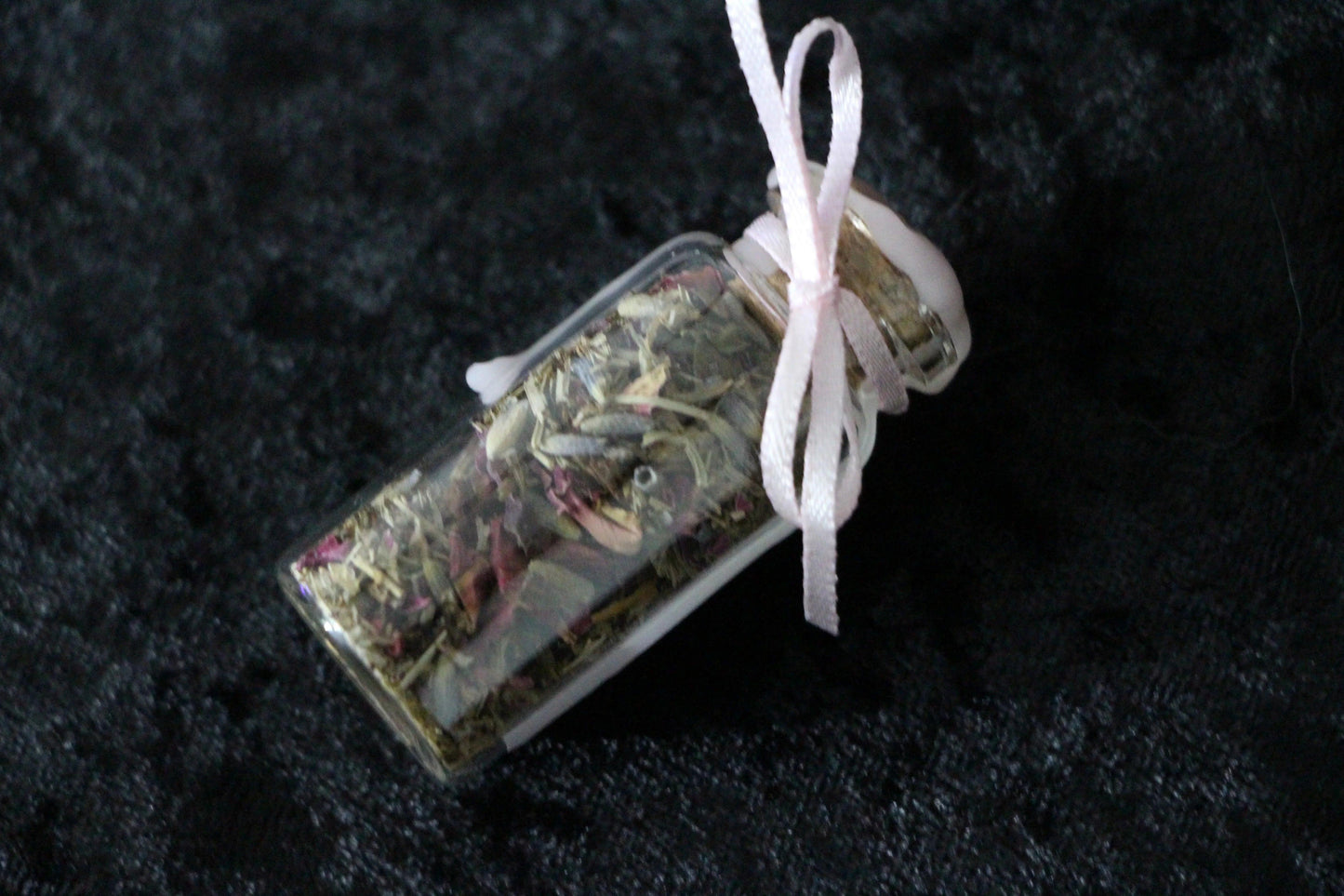 Glass jar filled with dried herbs, sealed with wax and a bow, on black fabric background