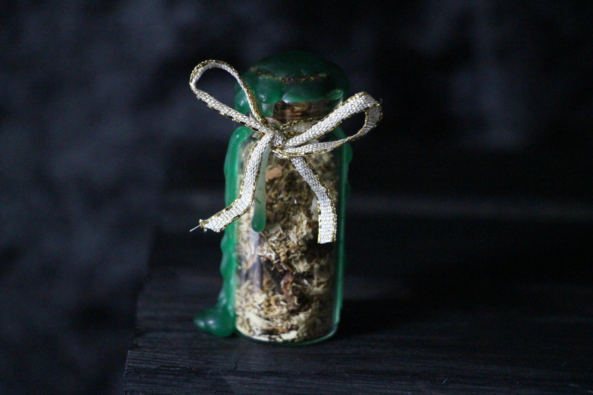 Herbal spell jar with green wax and gold ribbon, witchcraft ritual tool on dark background