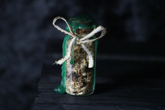 Herbal spell jar with green wax and gold ribbon, witchcraft ritual tool on dark background