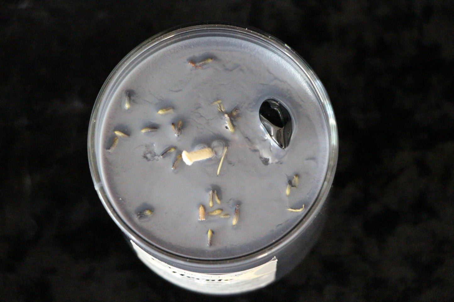 Top view of a lavender-scented black candle with dried lavender buds on a dark surface