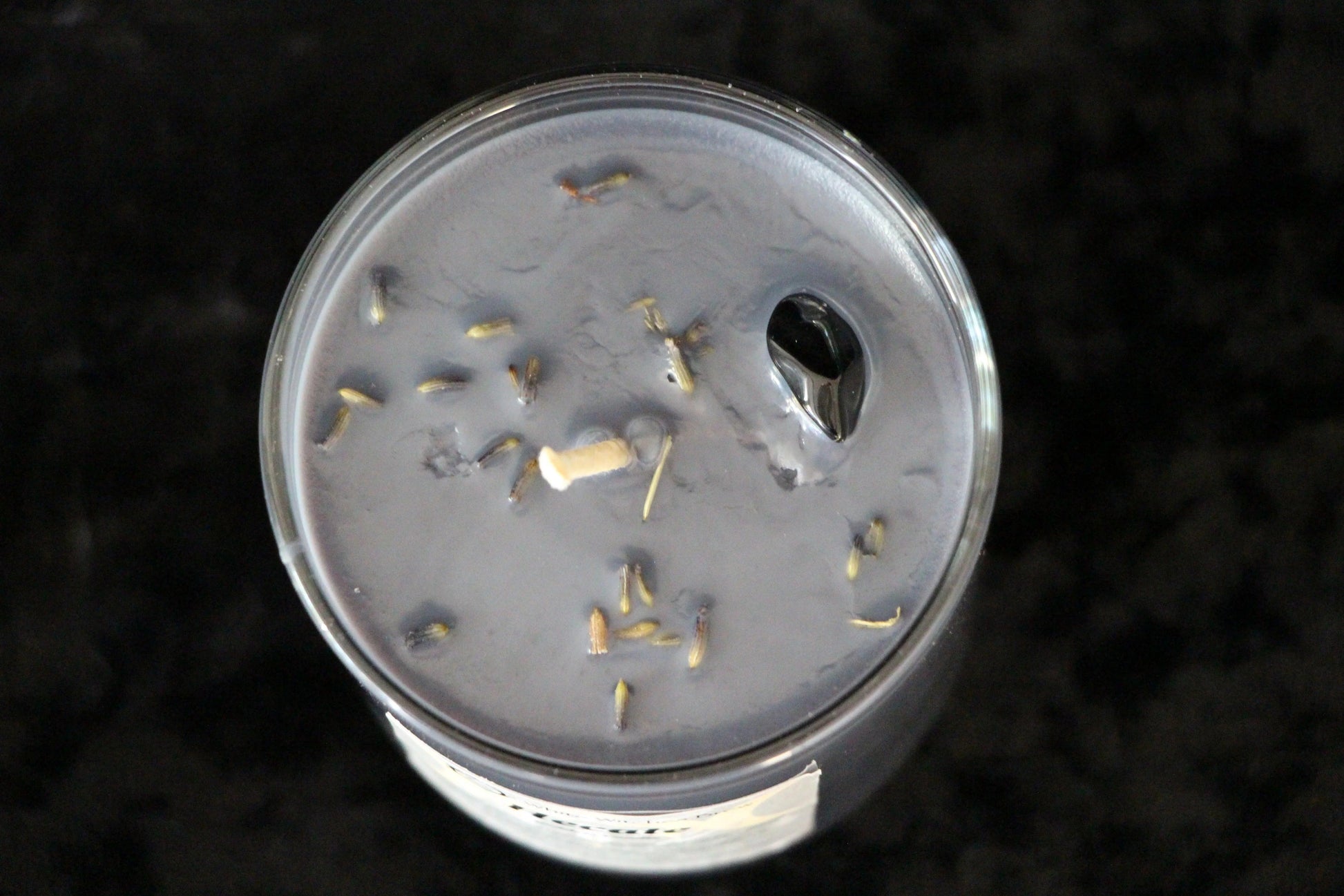 Top view of a lavender-scented black candle with dried lavender buds on a dark surface