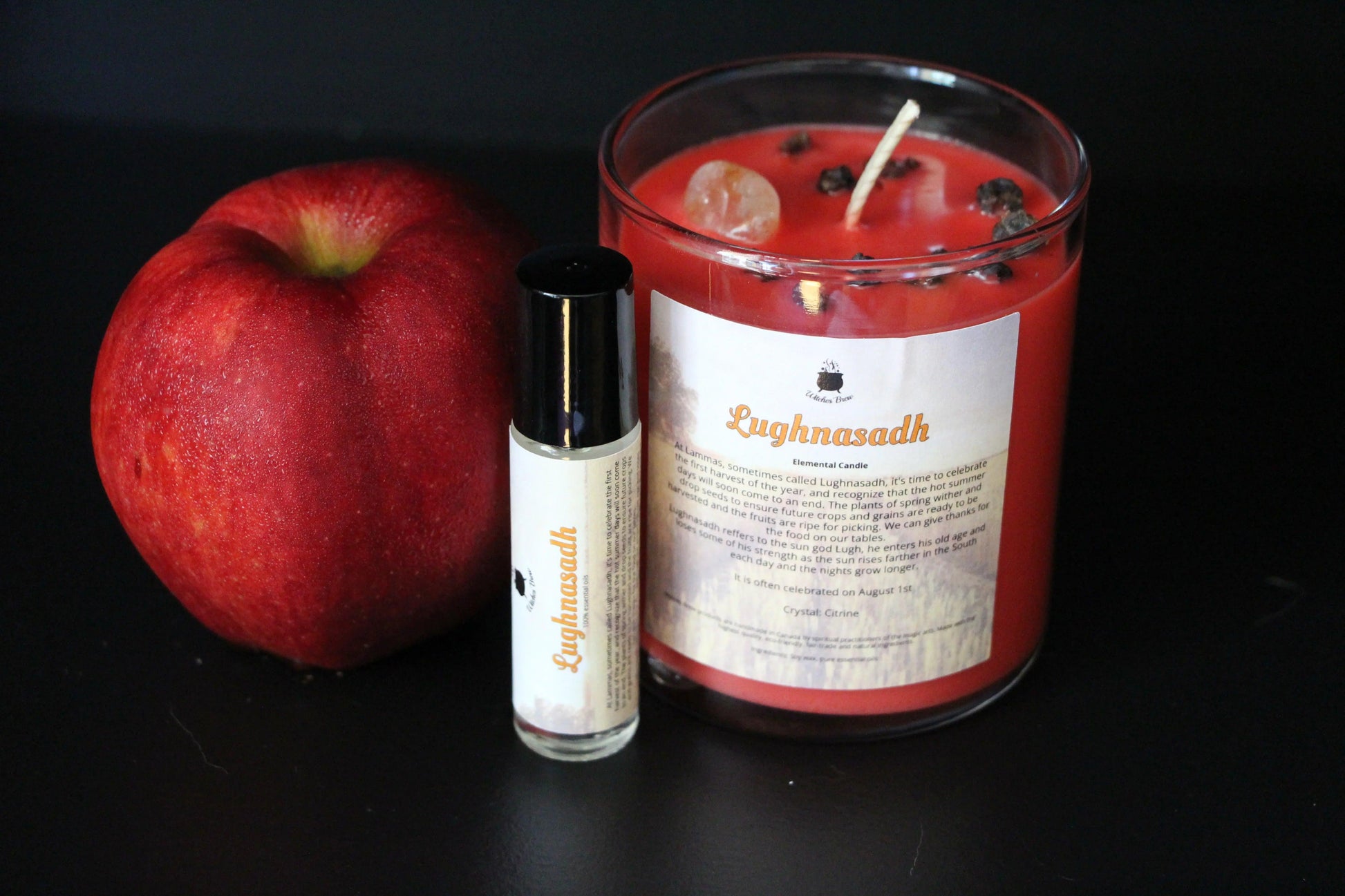Red Lughnasadh ritual candle, essential oil, and apple on black background, Witches' Brew