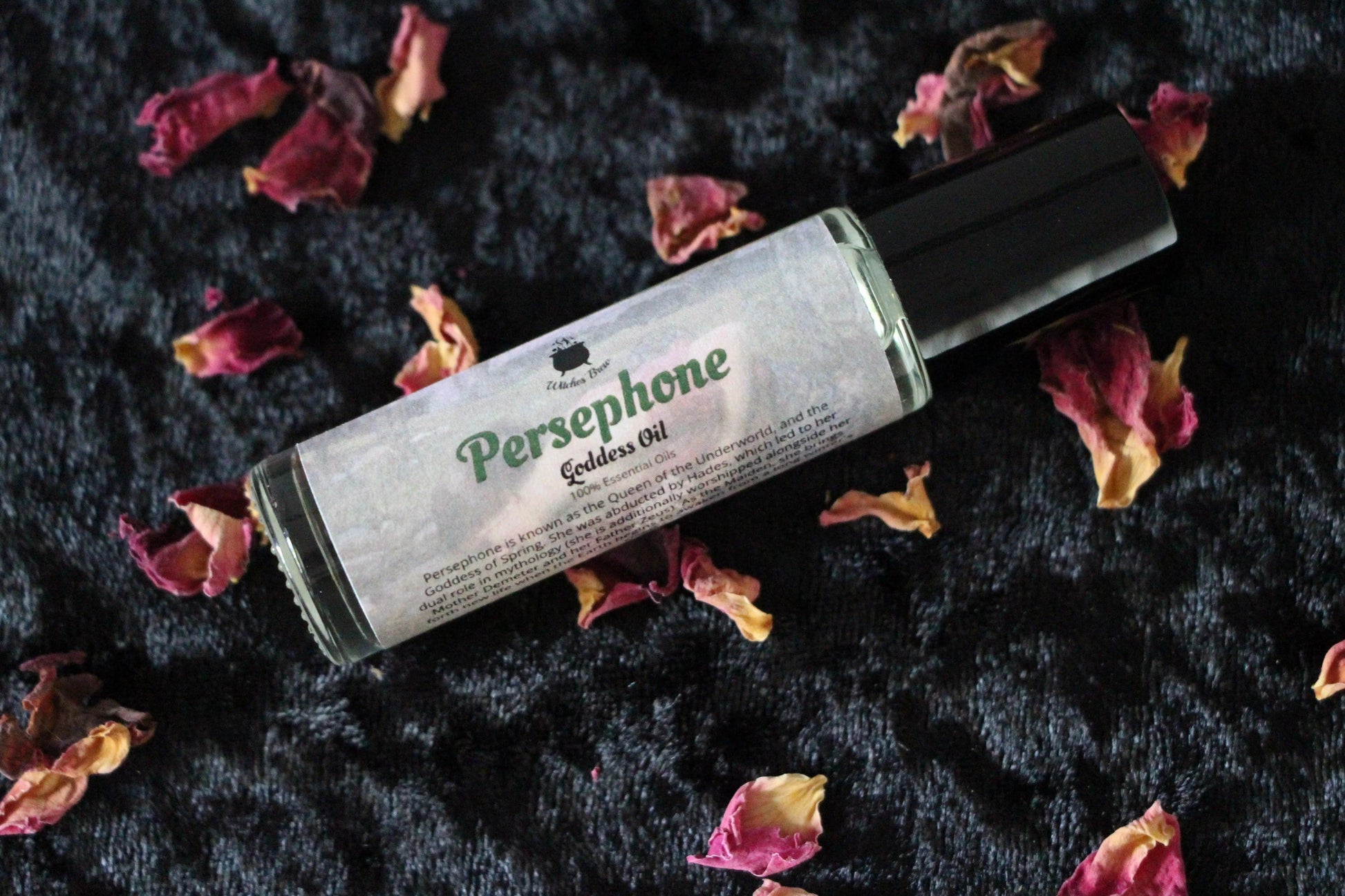 Persephone goddess oil bottle by Witches' Brew on black fabric with dried rose petals