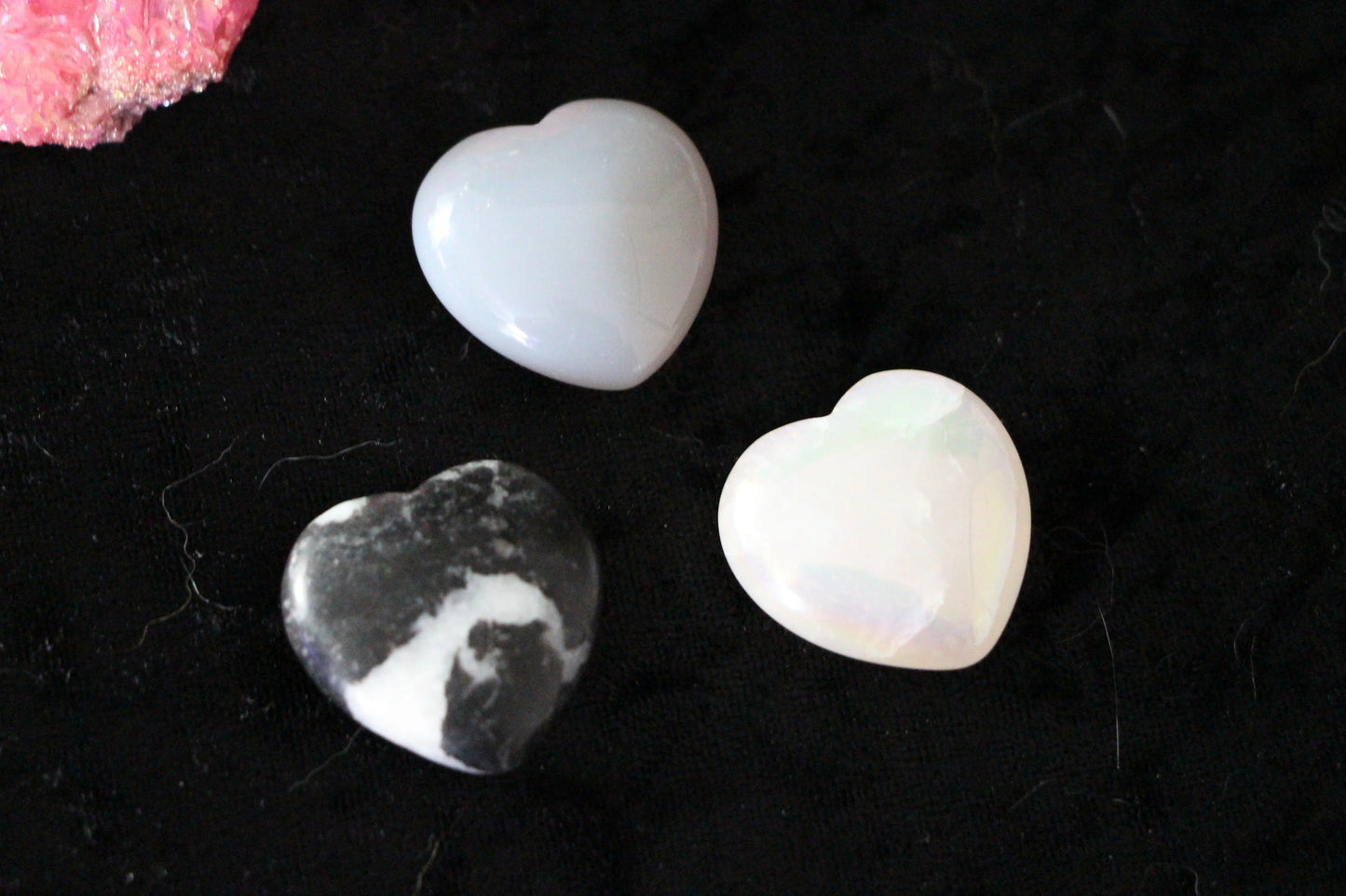 Three heart-shaped crystal stones on black fabric, ideal for modern witch ritual tools