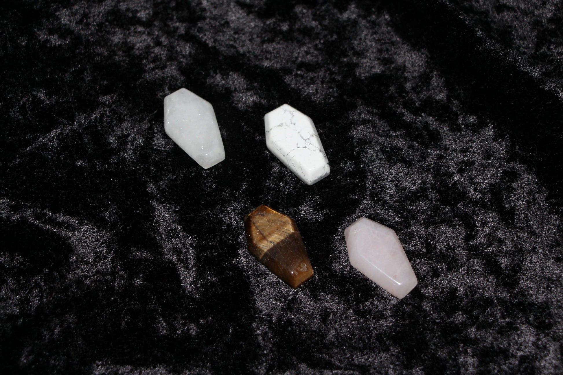 Four coffin-shaped crystal stones on black velvet, modern witch ritual tools