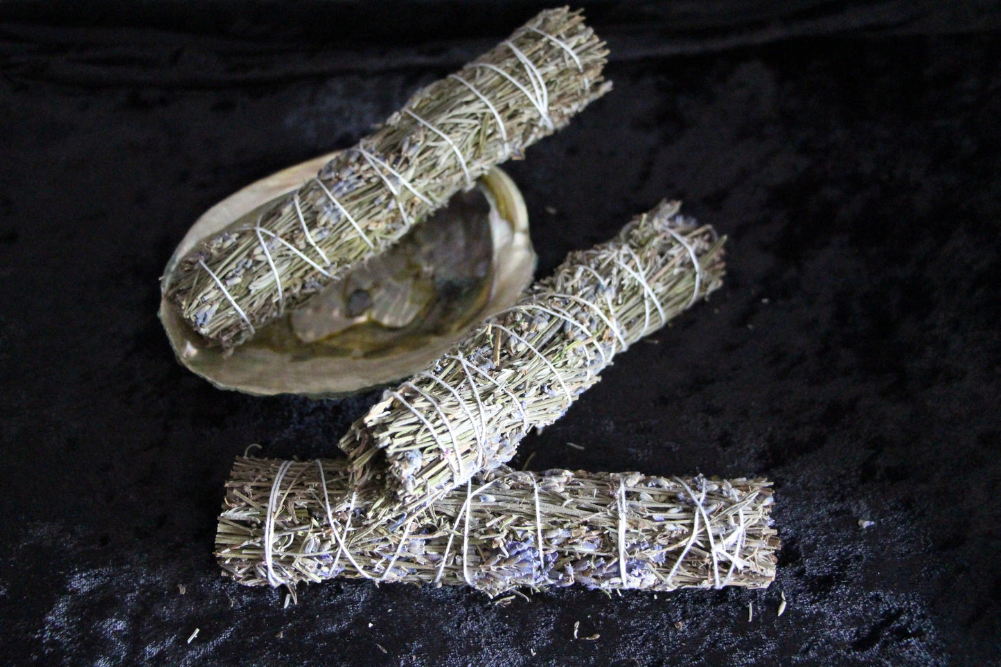 Hand-crafted sage bundles and abalone shell on black cloth, ritual tools for modern witches.