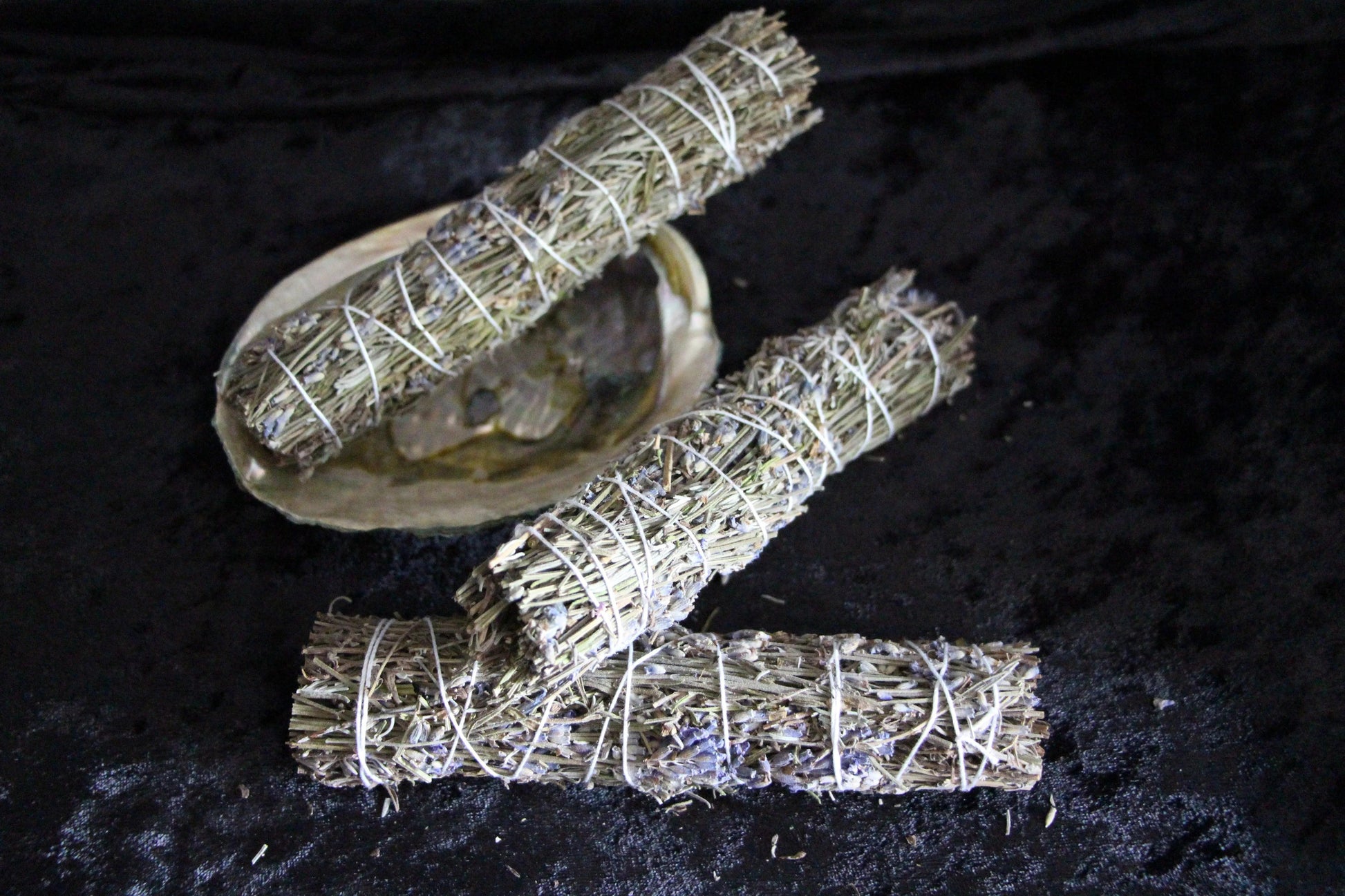 Hand-crafted sage bundles and abalone shell on black cloth, ritual tools for modern witches.