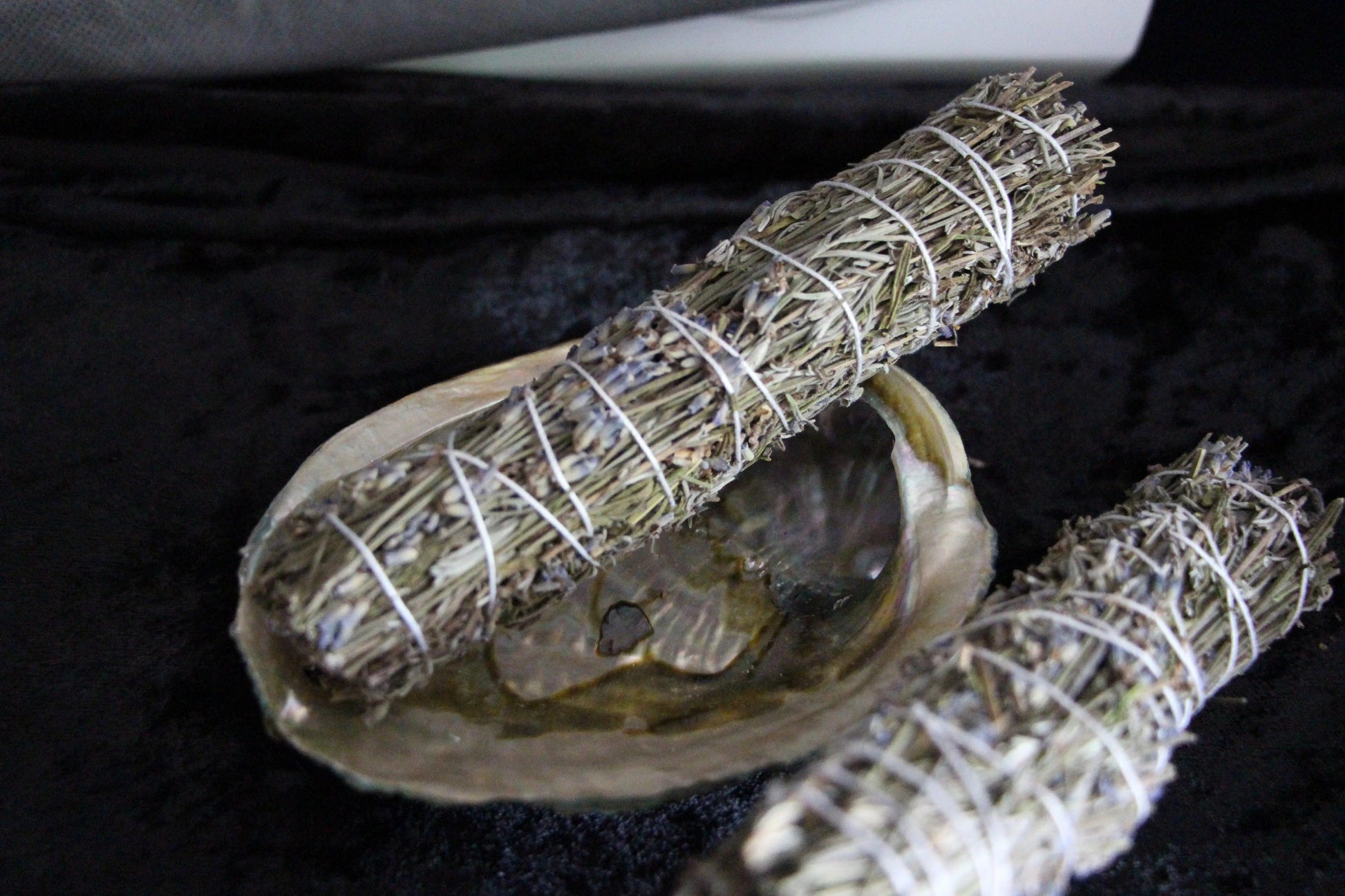 Handcrafted sage bundles with lavender in abalone shell on black velvet for ritual cleansing