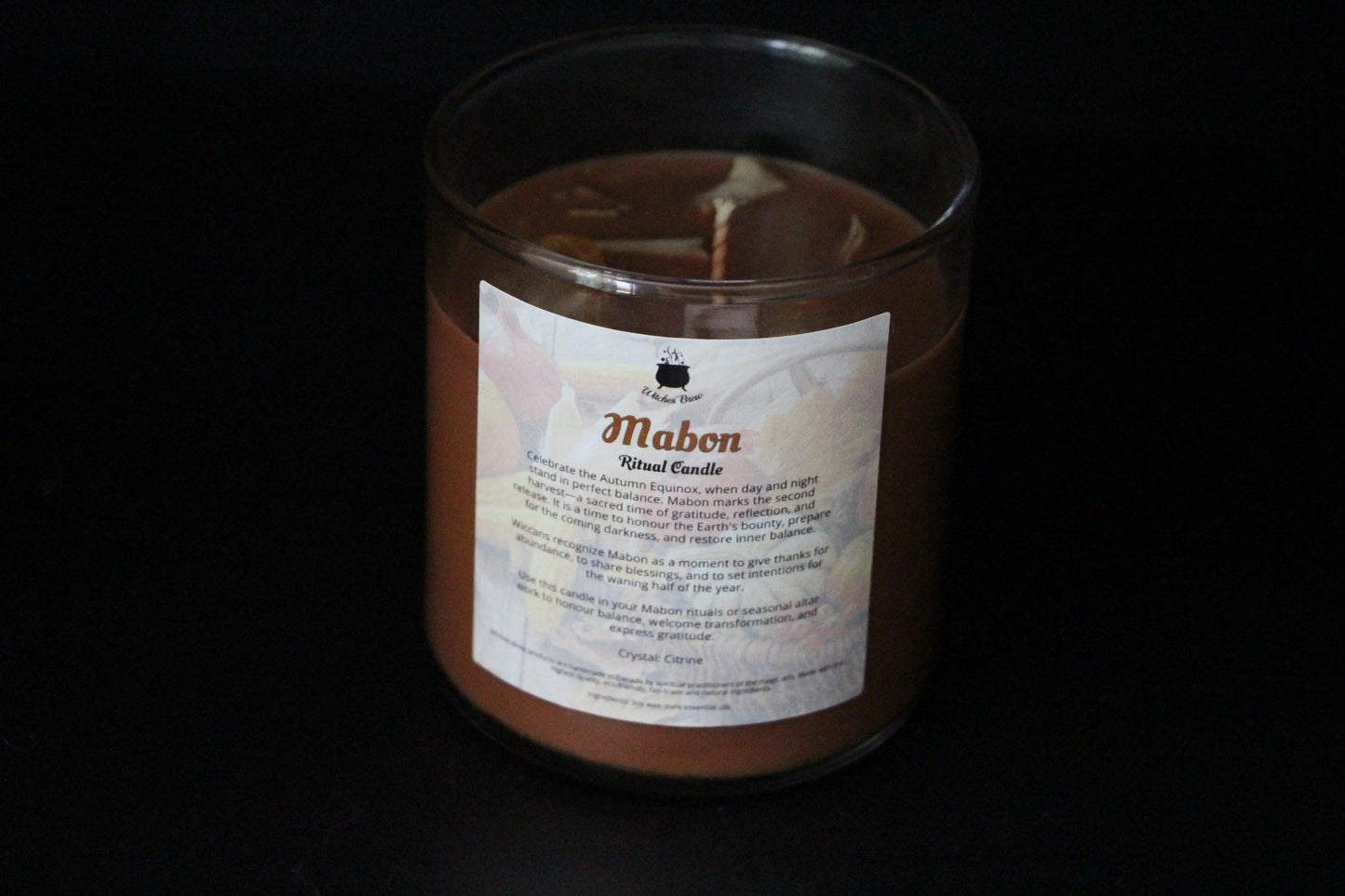 Mabon ritual candle in glass jar, labeled Witches' Brew, against black background