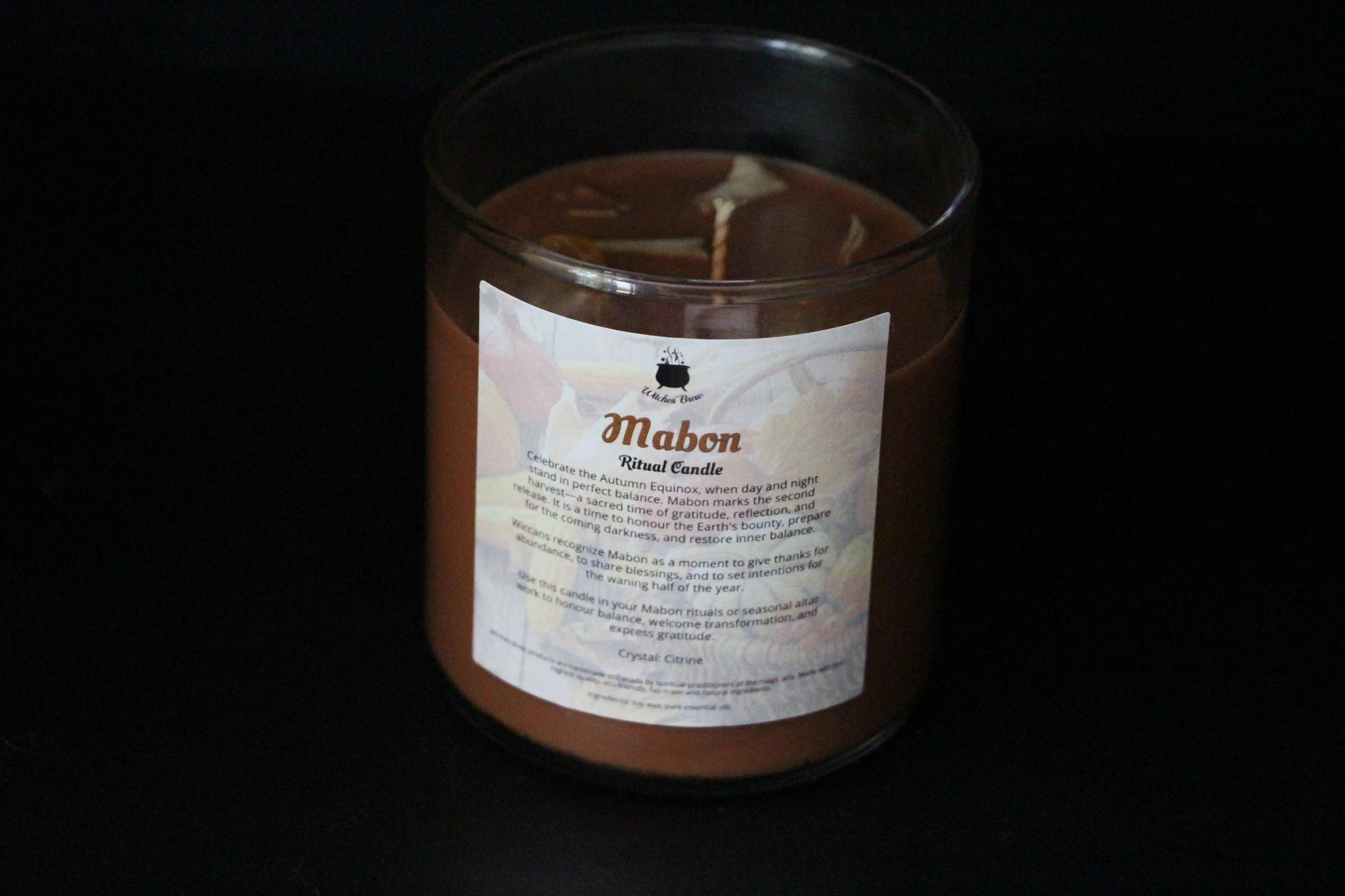 Mabon ritual candle in glass jar, labeled Witches' Brew, against black background