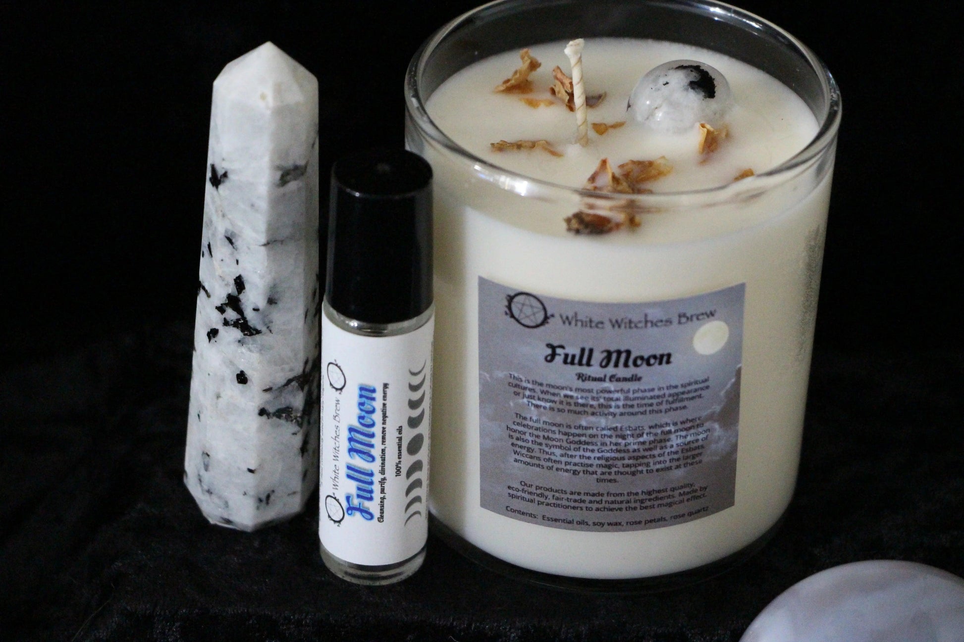 Full Moon ritual candle, essential oil roller, and black and white crystal on black cloth