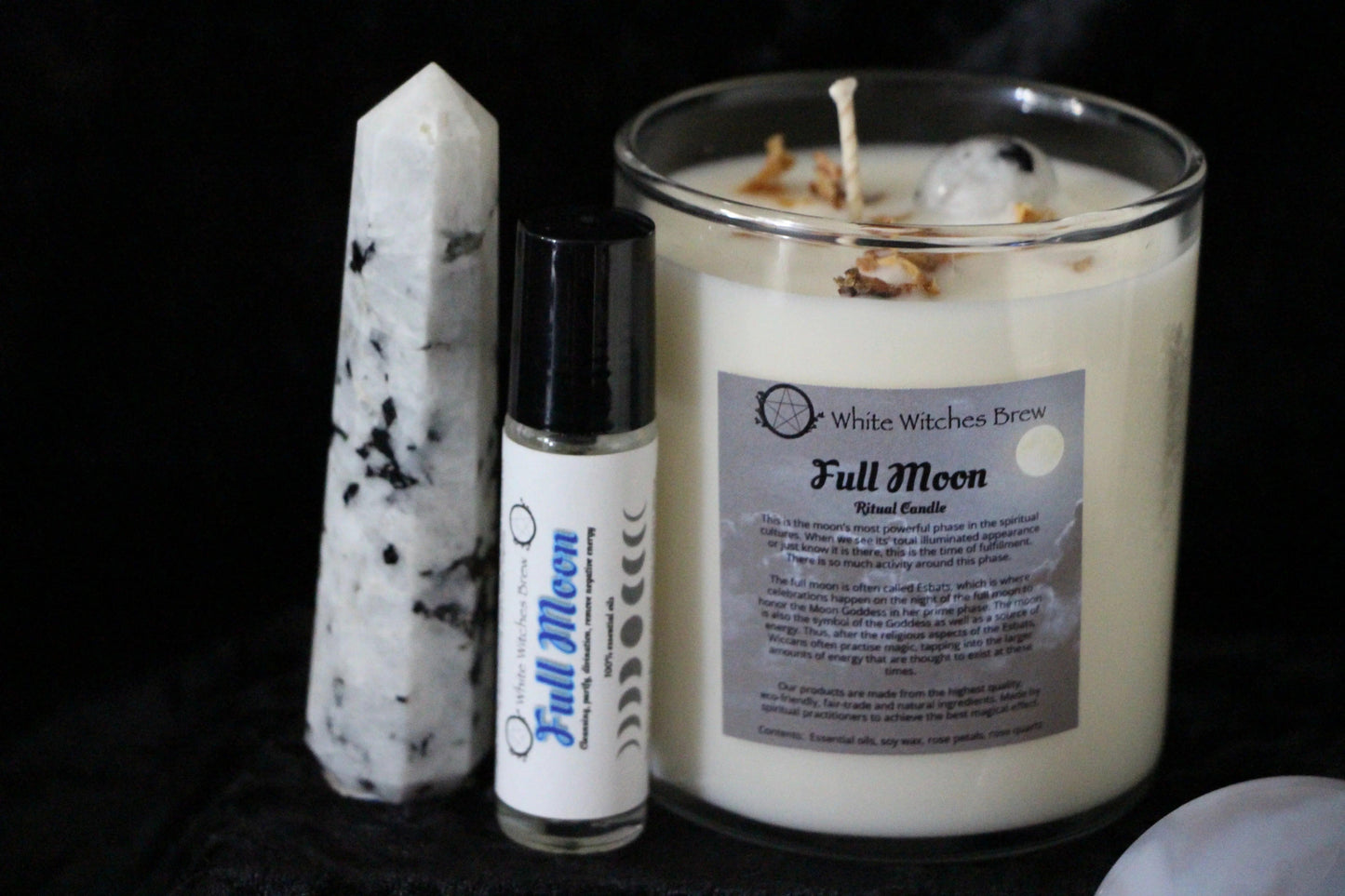 Full Moon ritual candle and essential oil roller with white and black speckled crystal on black background