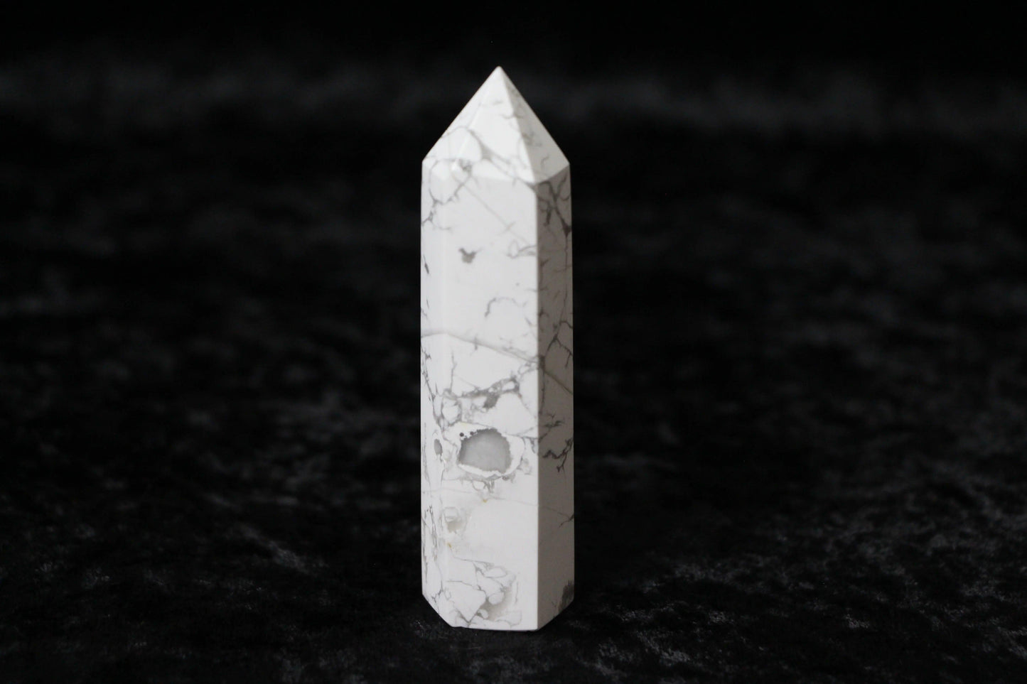 White howlite crystal point with gray veining on black textured surface