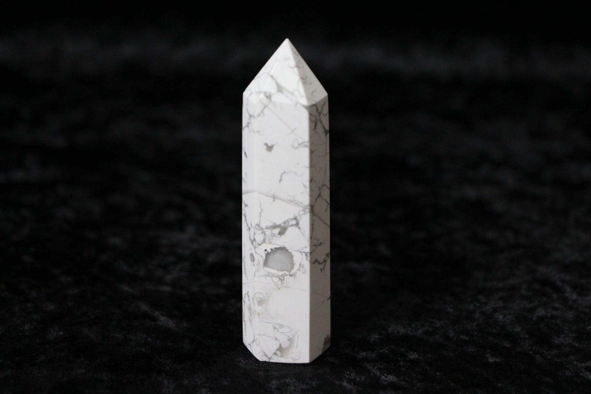 White howlite crystal point with gray veining on black textured surface