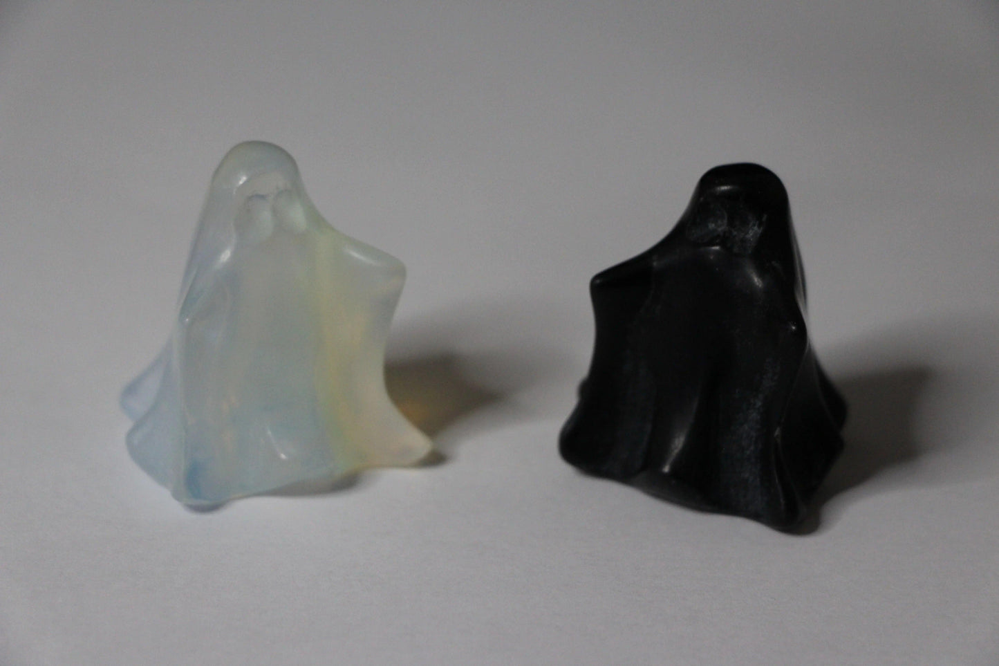 Opalite and obsidian crystal ghost figurines on a white background