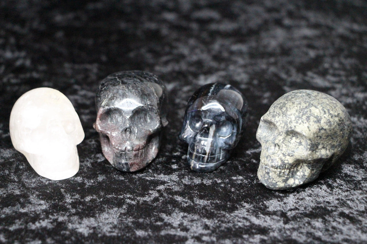 Four carved crystal skulls in different stones on a dark textured background