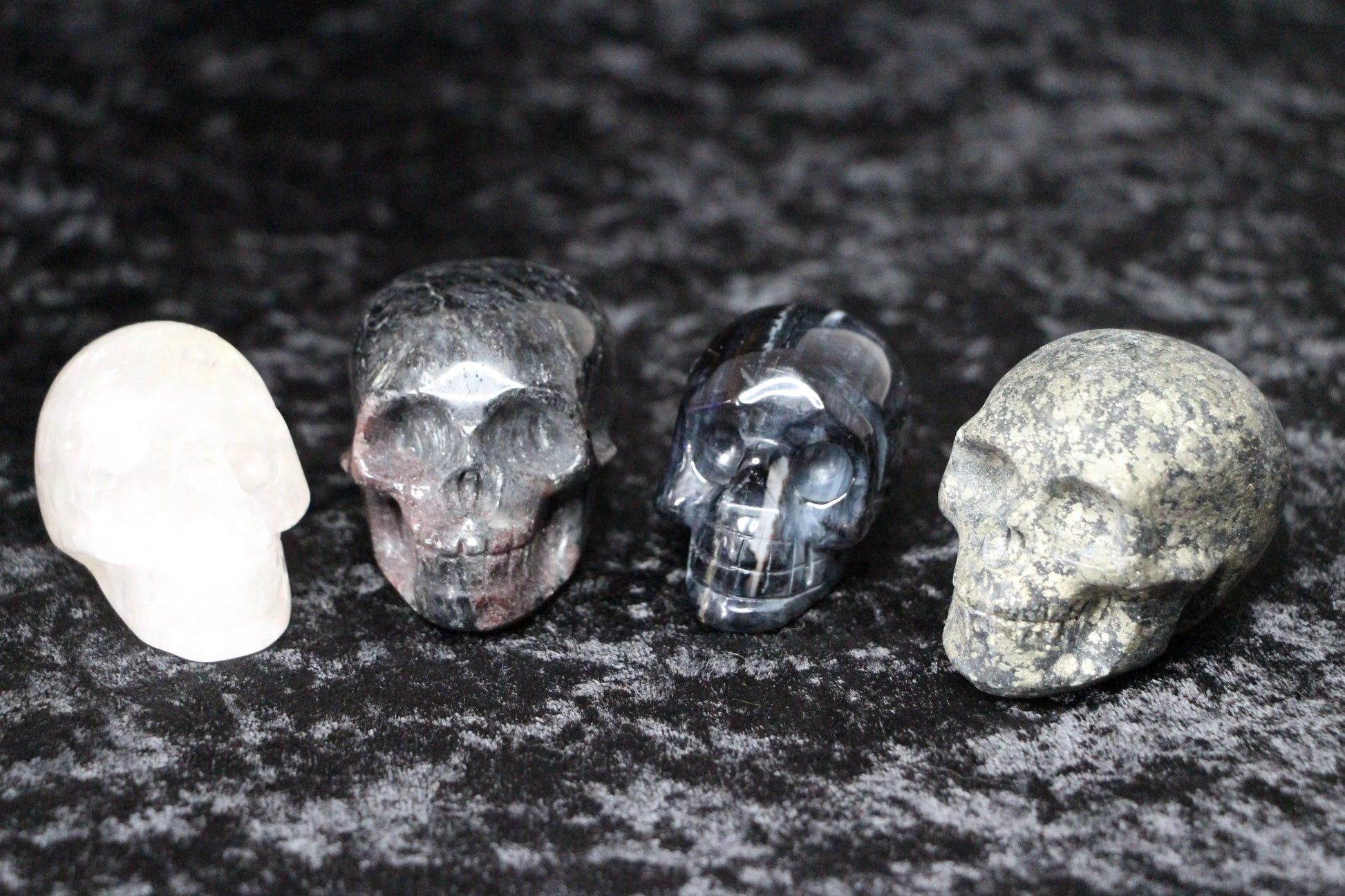 Four carved crystal skulls in different stones on a dark textured background