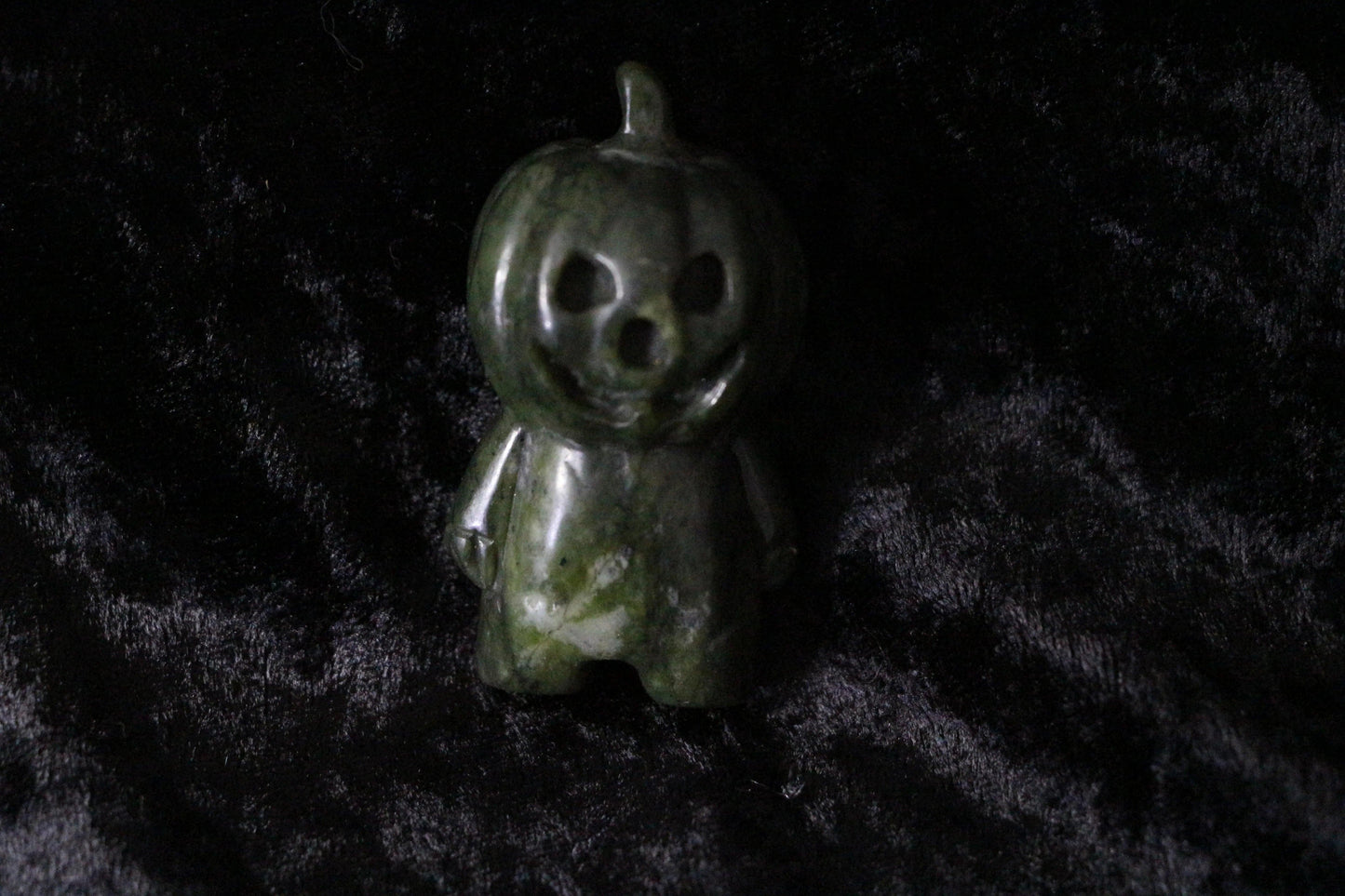 Green jade pumpkin figurine with carved face on black velvet background