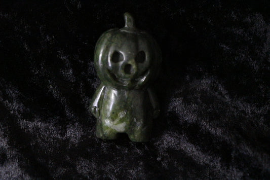 Green jade pumpkin figurine with carved face on black velvet background