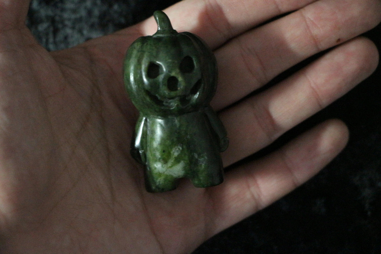 Small green jade pumpkin figurine with carved jack-o'-lantern face held in hand