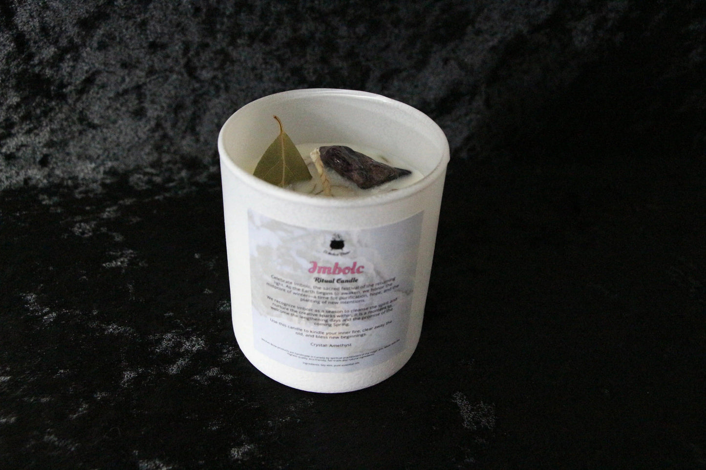 Imbolc ritual candle with bay leaf and crystal on white wax, set against black fabric