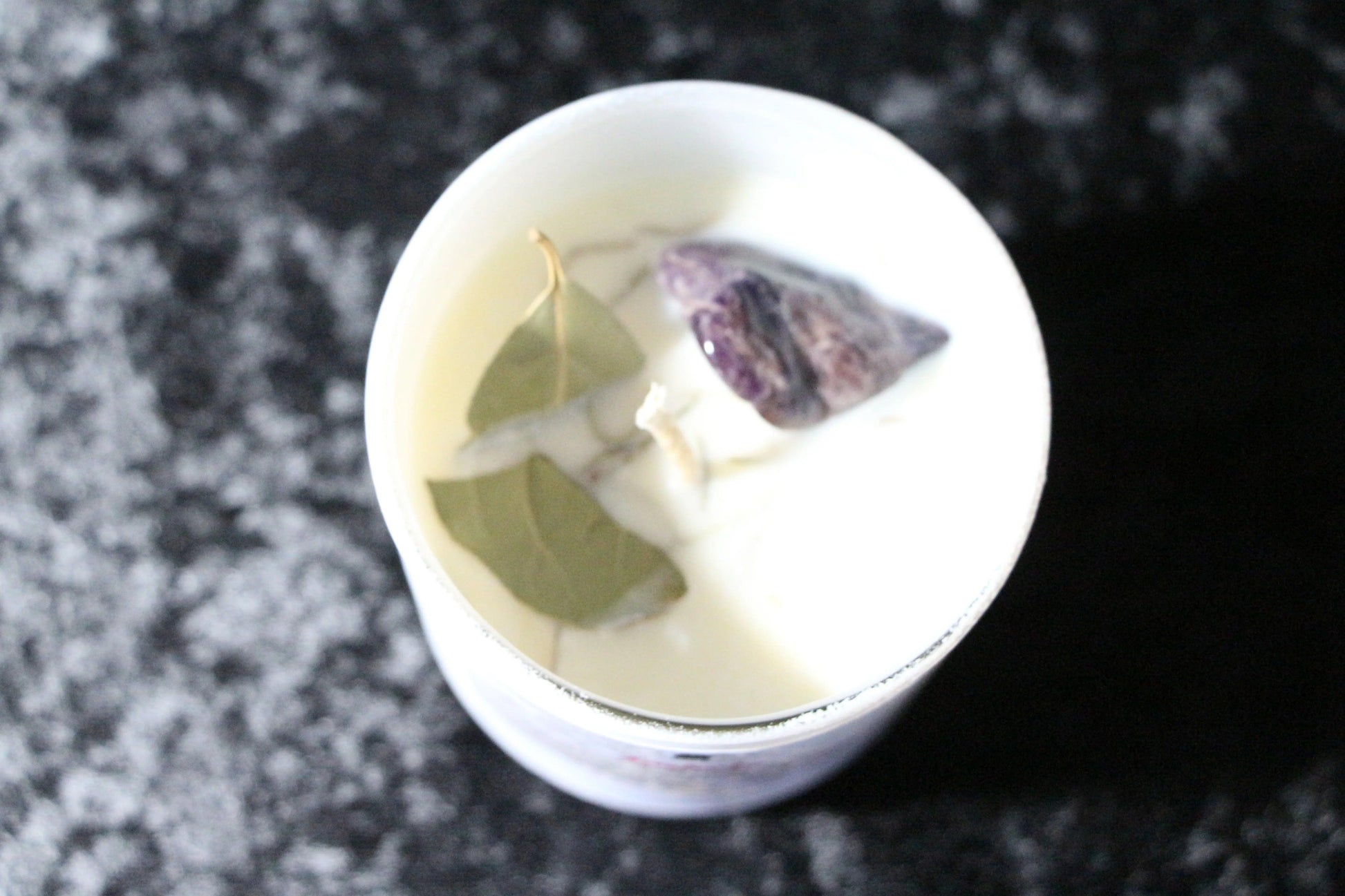 Crystal candle with herbs and amethyst on black textured background