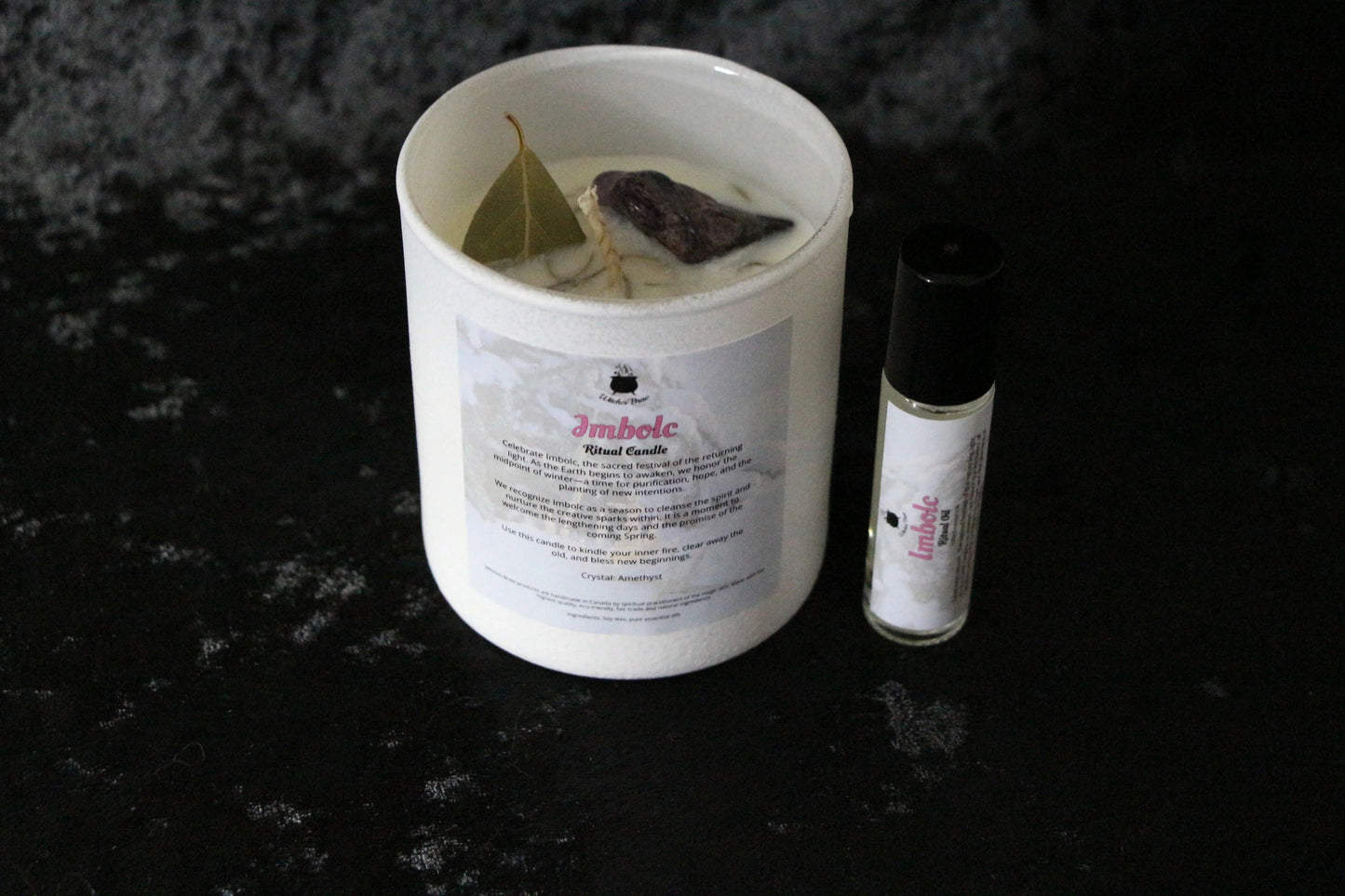 Imbolc ritual candle with crystal and bay leaf, paired with essential oil roller on dark background