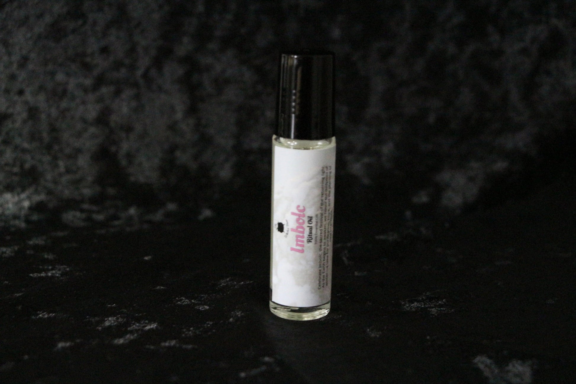 Imbolc ritual oil bottle with black cap on textured dark background