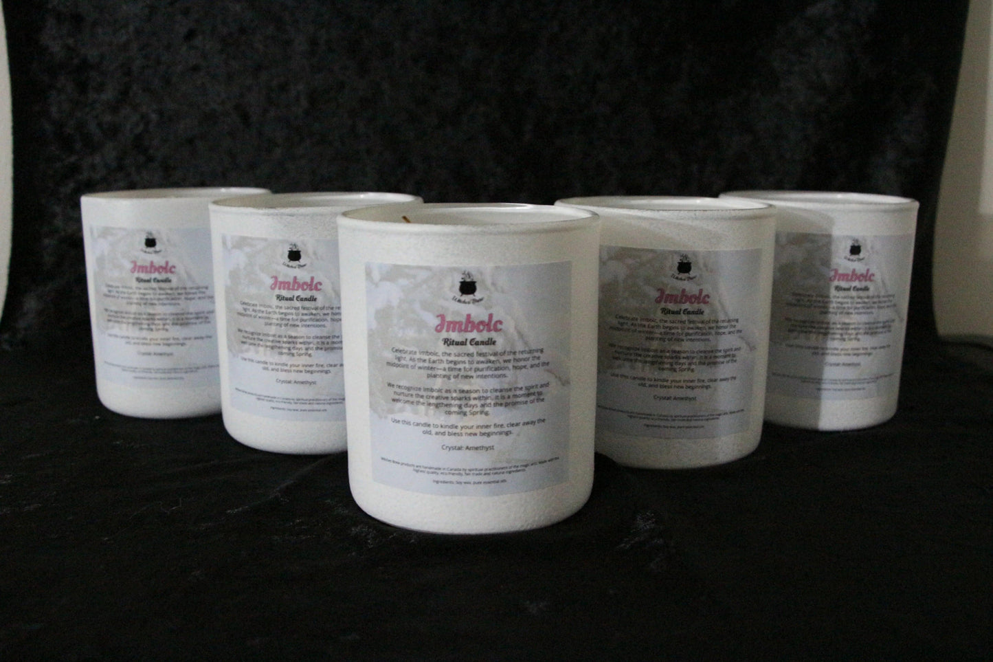 Hand-crafted Imbolc ritual candles in white glass jars on a black background