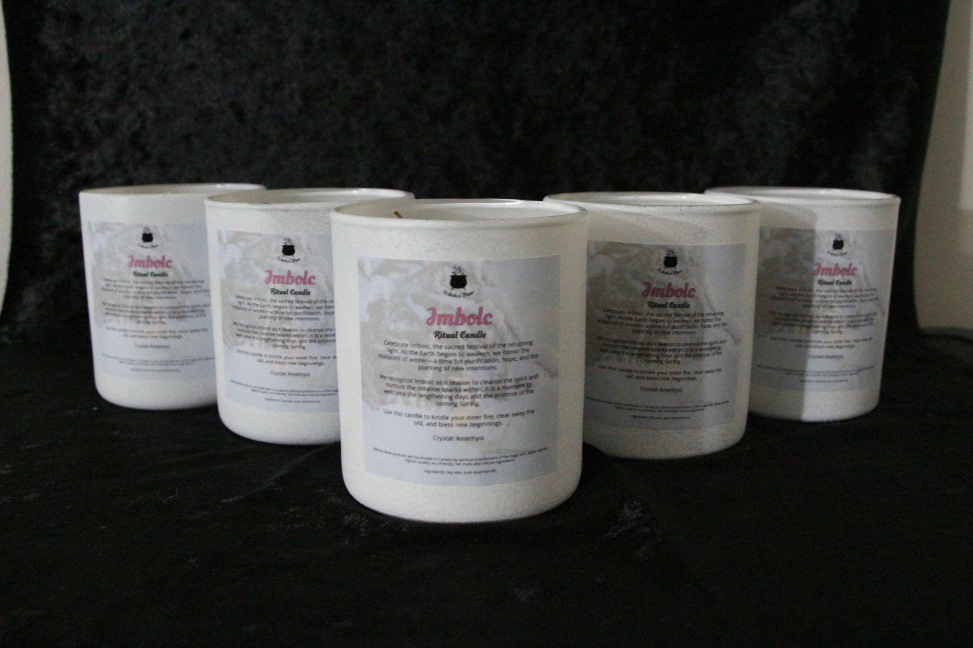 Hand-crafted Imbolc ritual candles in white glass jars on a black background