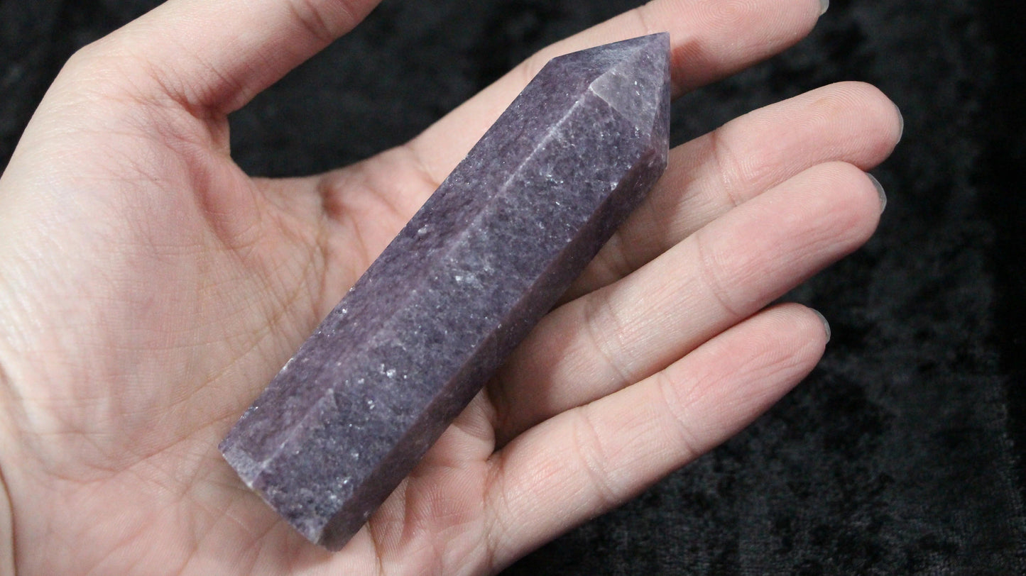 Hand holding a polished purple lepidolite crystal point against a dark background