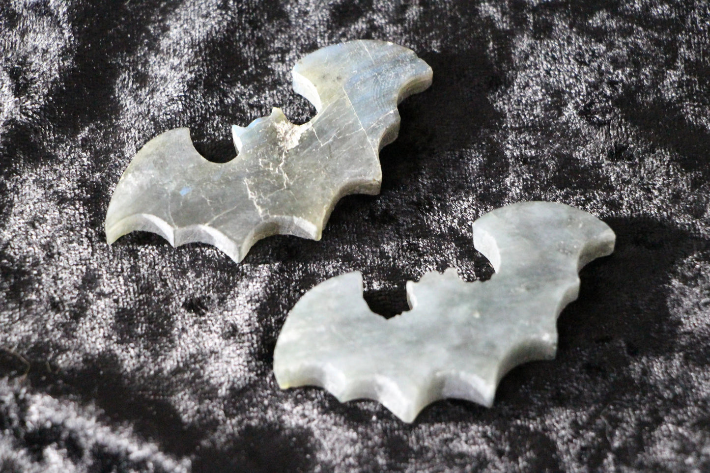 Two labradorite crystals carved into bat shapes on black velvet fabric