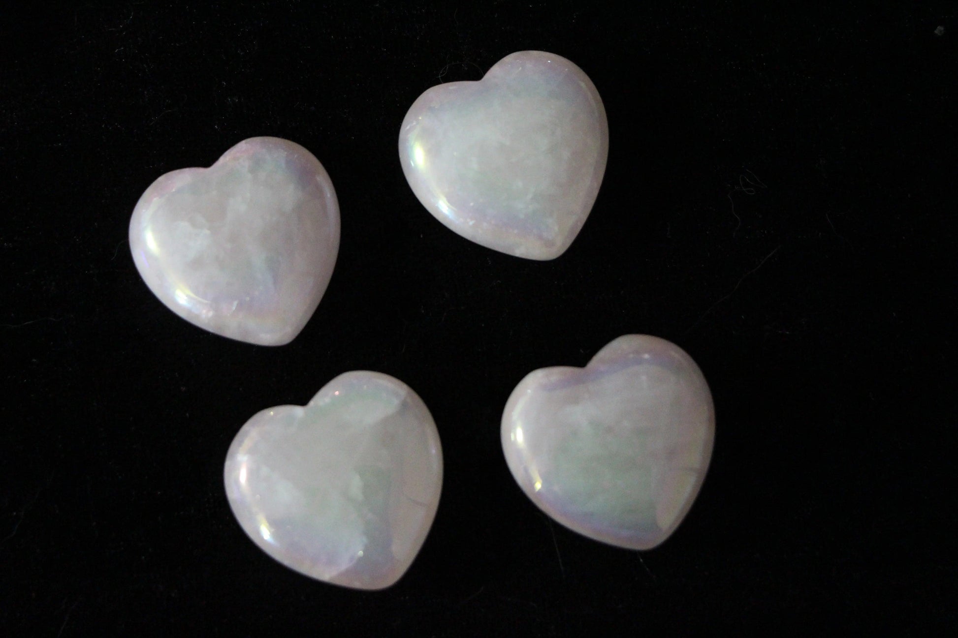 Four polished pink aura rose quartz heart crystals on a black background