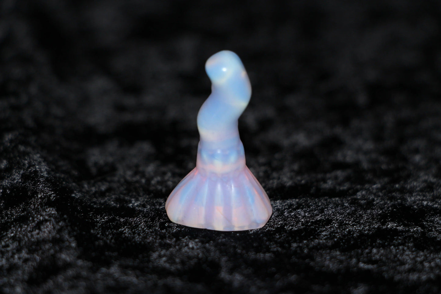 Pink opalite crystal figurine for witchcraft rituals on black velvet background