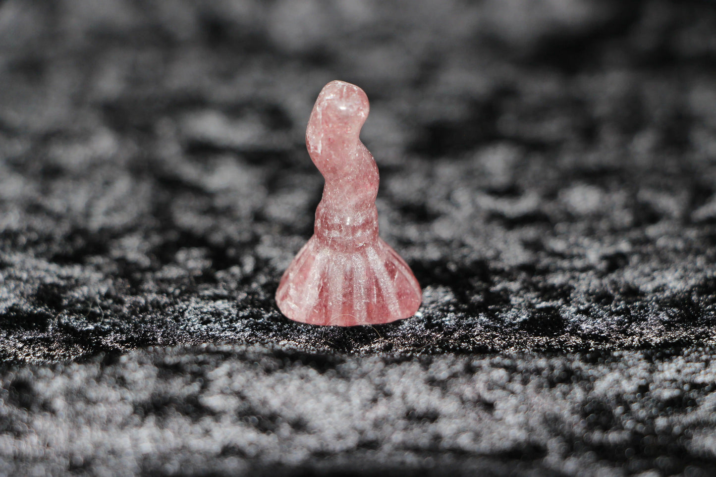 Hand-carved strawberry quartz crystal witch figurine on black textured background