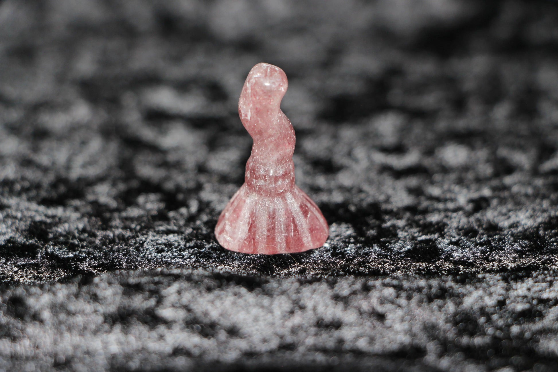 Hand-carved strawberry quartz crystal witch figurine on black textured background