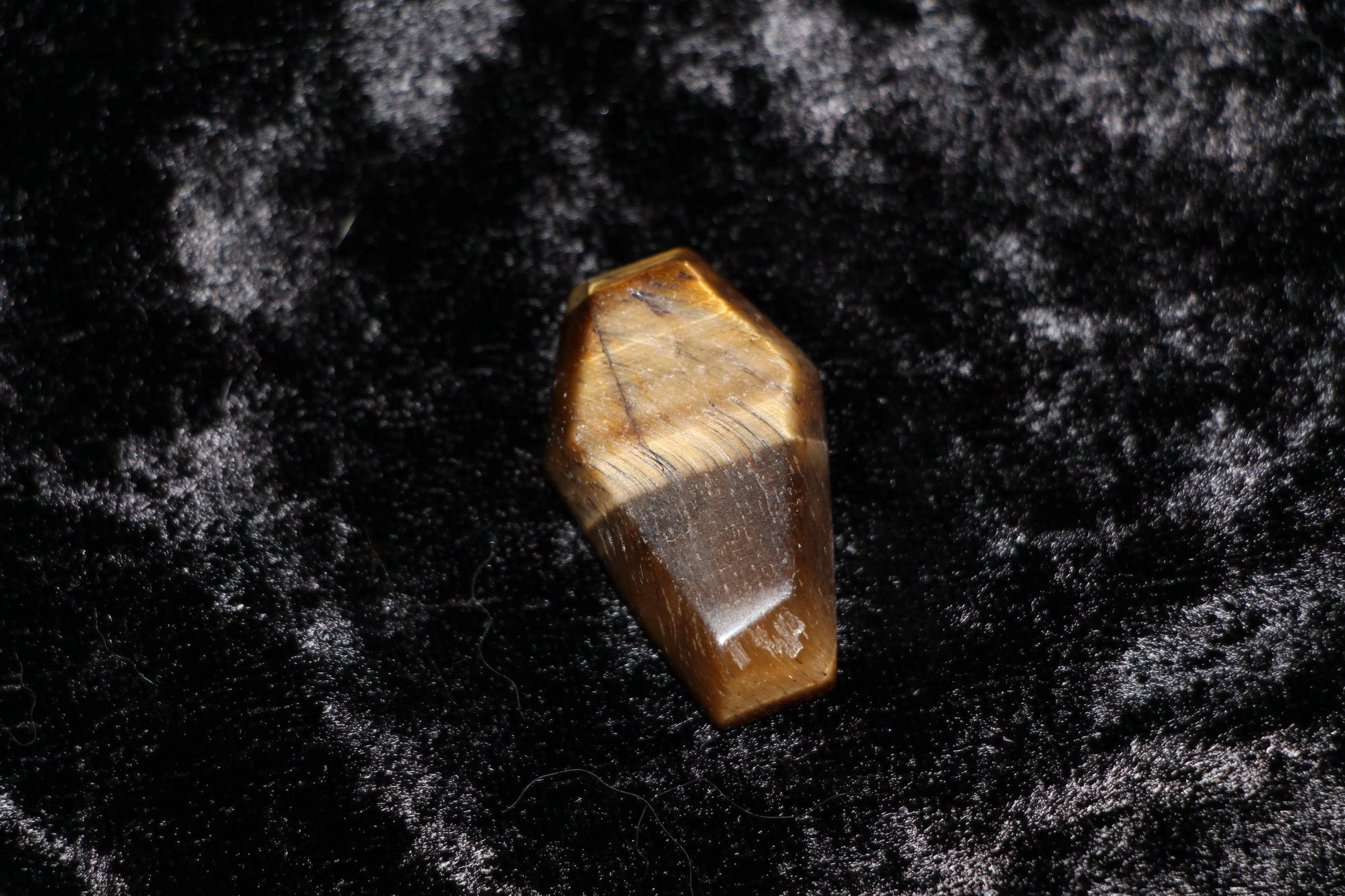 Polished tiger's eye crystal coffin on black velvet, ritual tool for modern witch